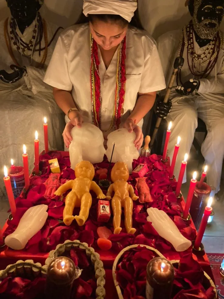 Mãe Jassiara com as mãos sobre o altar de pétalas de rosa, velas vermelhas e imagens de cera