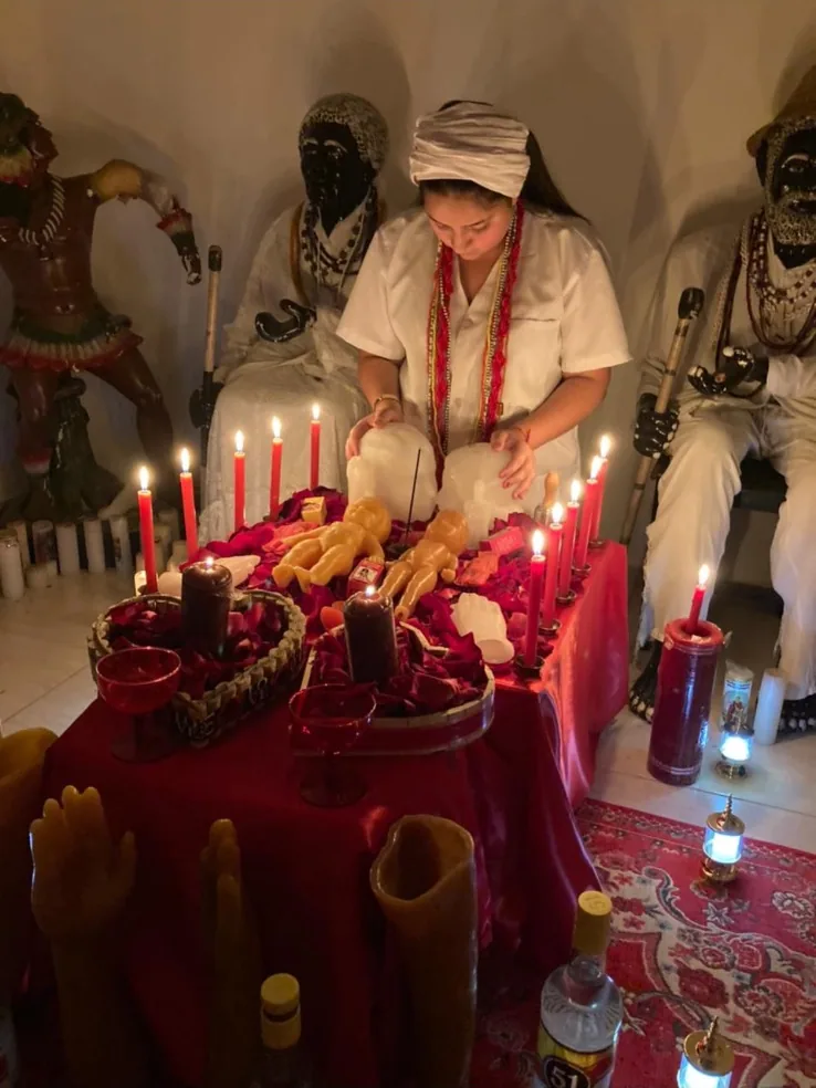 Mãe Jassiara diante da mesa vermelha com velas, entre as imagens da casa de santo
